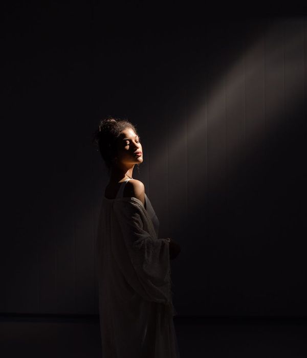 Person in a flowing yoga pose in a minimalist, dark room.